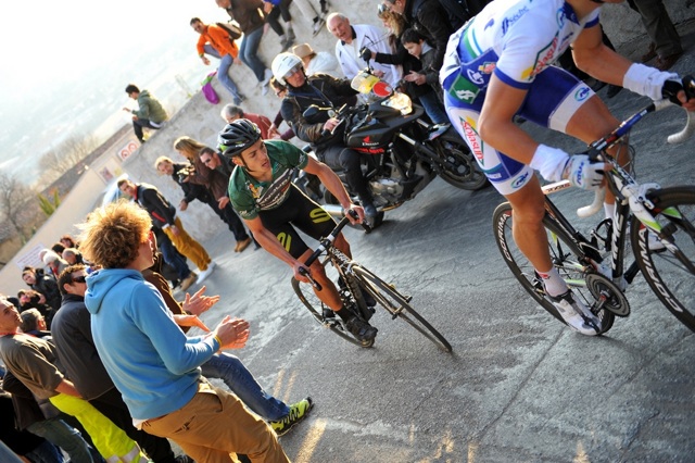 Jon Tiernan-Locke in the green jersey of leader of the Haut Var race, cycling up a very steep hill cheered on by crowds