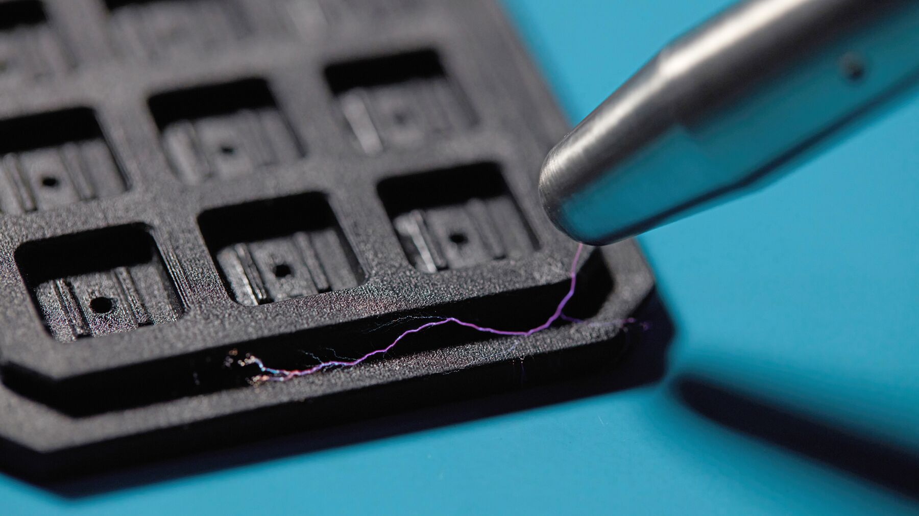 Tweezers lifting a small electronic component out of a black component nest printed in Formlabs ESD Resin