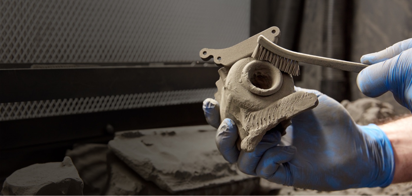 Technician hand-brushing loose powder off a Nylon 12 SLS part during standard media-blast post-processing