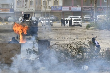 Protesters take cover after throwing a Molotov cocktail at riot police in an armoured personnel carrier during early morning clashes, on the fourth anniversary of an uprising, in the village of Sanabis