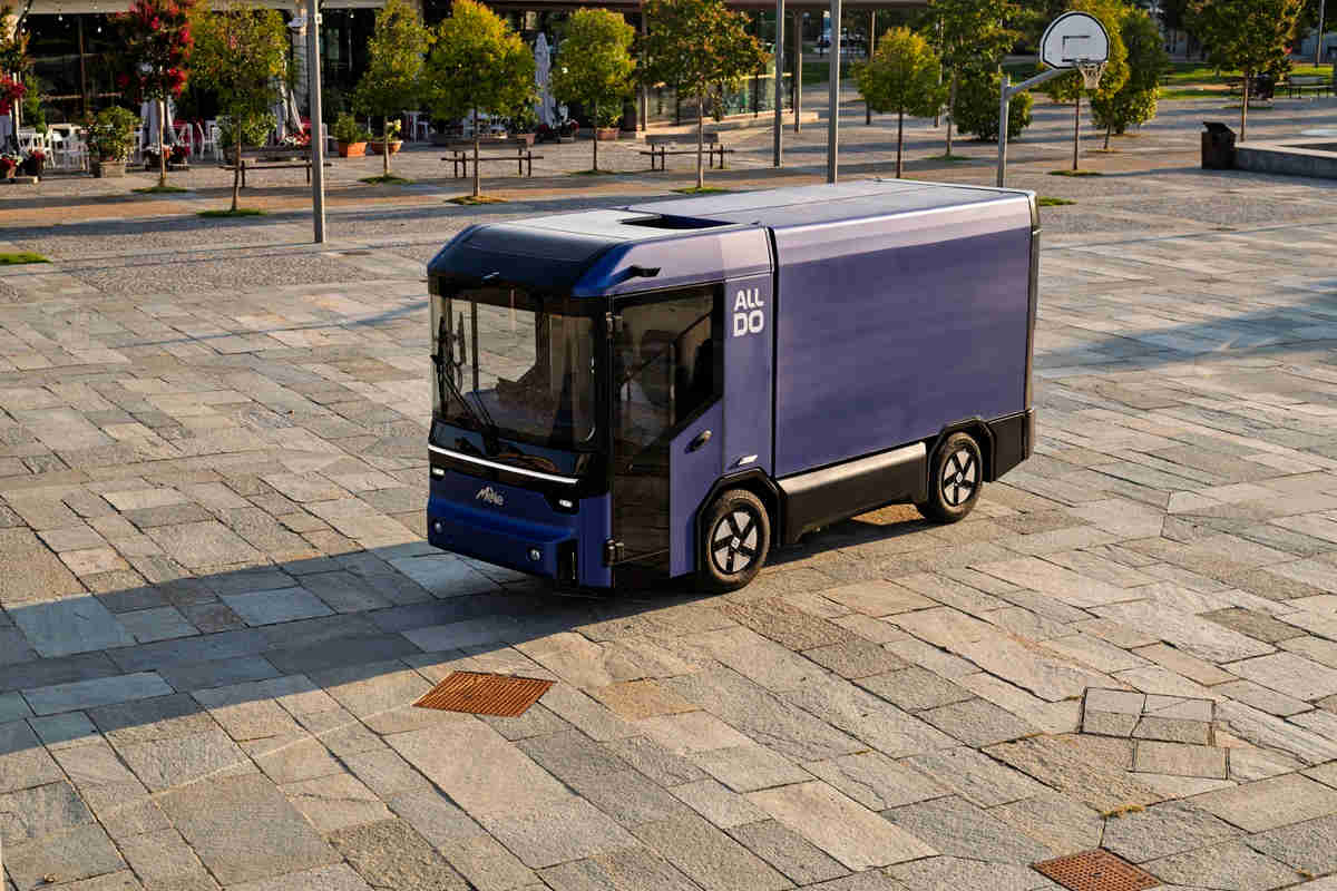Un veicolo elettrico modulare in movimento, con cabina avanzata e spazio di carico, in un contesto urbano
