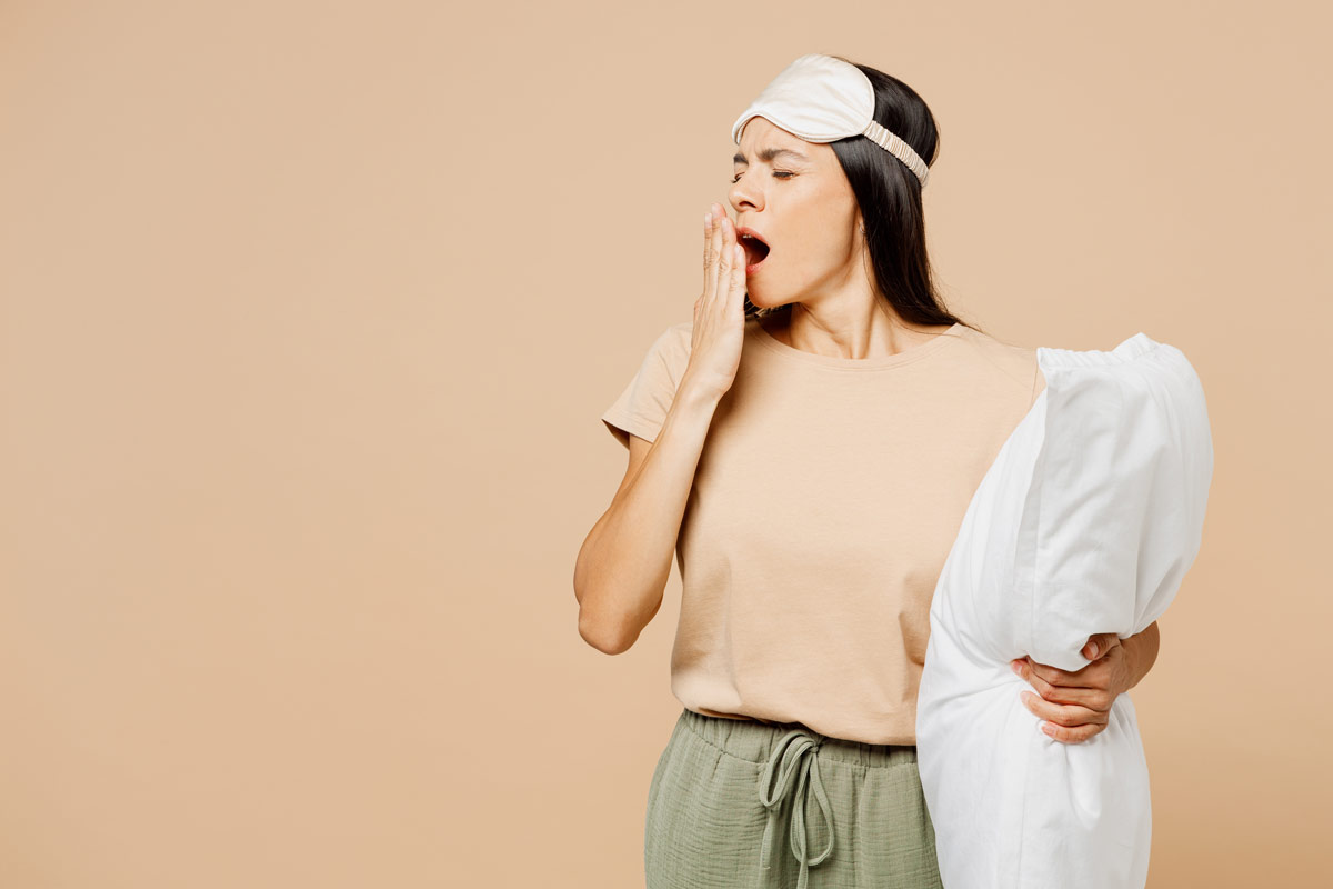 Sleepy woman holding pillow and yawning