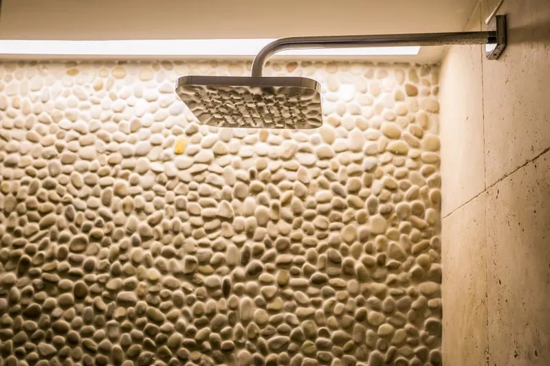 Rústico e moderno: banheiro combina seixos com mármore travertino