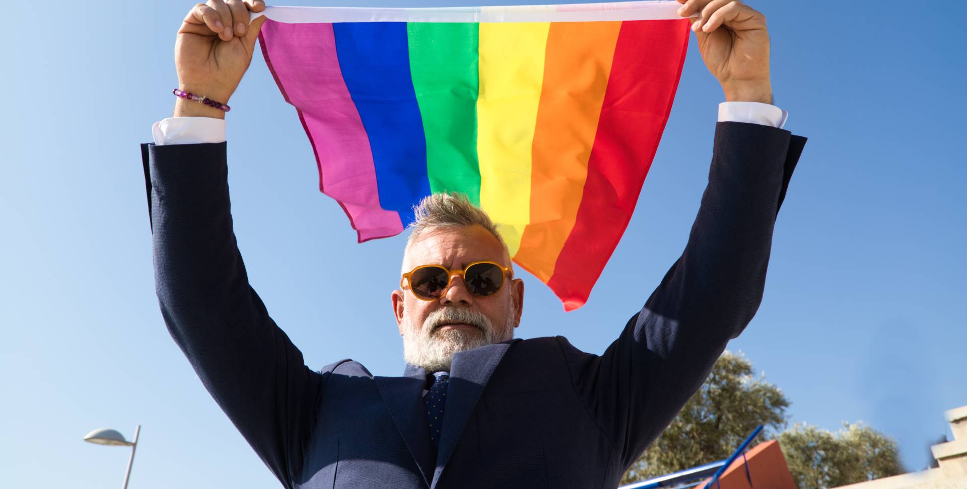 senior man proudly holding a pride flag in the air