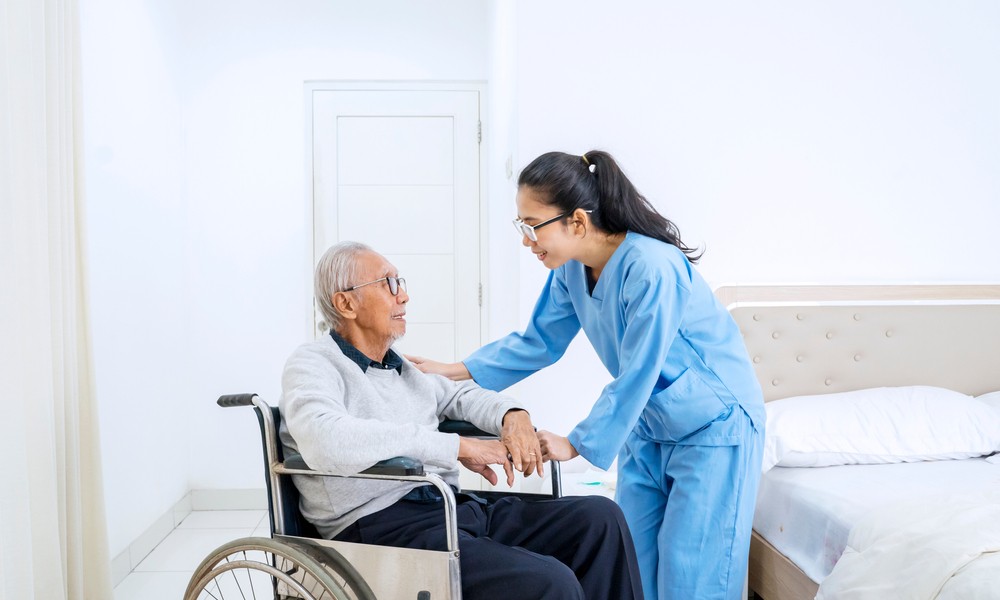 senior man sitting on the wheelchair while talking with young nurse