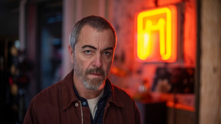 james nesbitt in front of a neon sign in Suspct