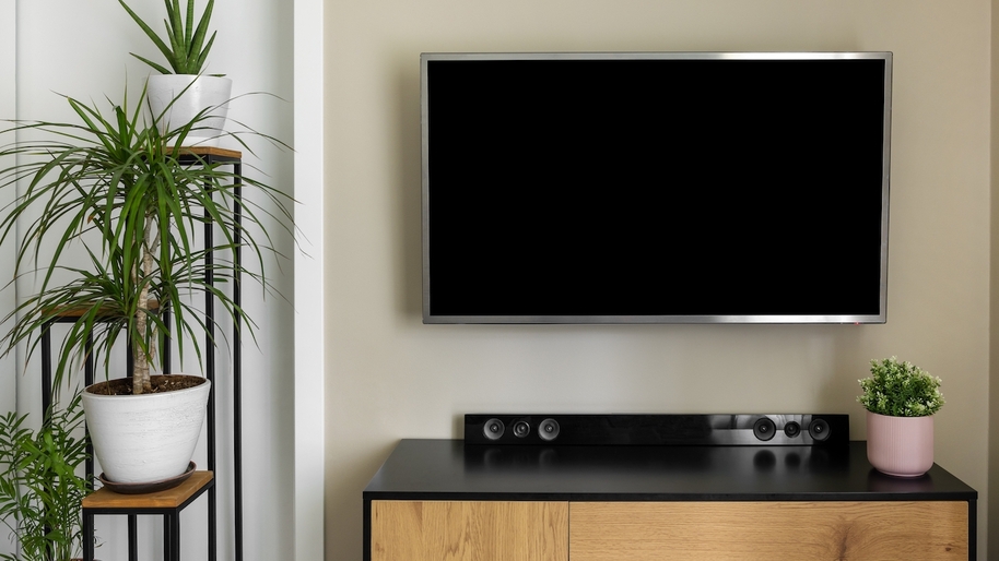 smart tv with soundbar hanging on beige wall in modern interior with green plants