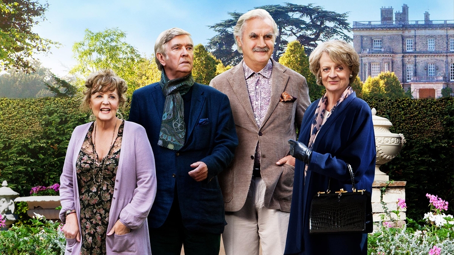 Four people stood in the foreground with greenery and an old building in the background