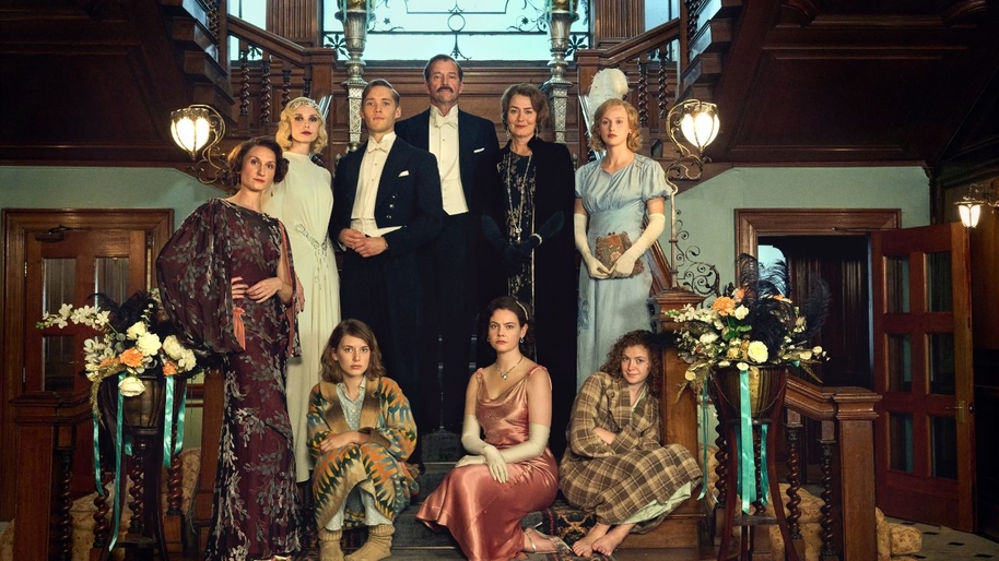 Aristocratic men and women in 1930s evening dresses and suits stood on a grand staircase