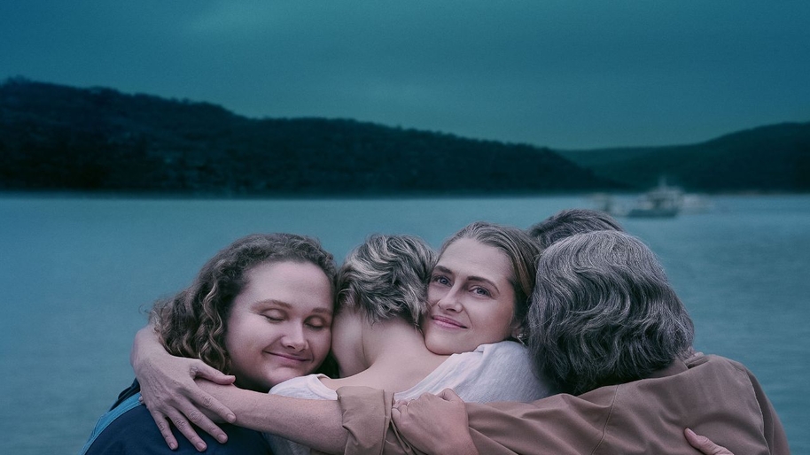 Four women of different ages hugging against the backdrop of a lake