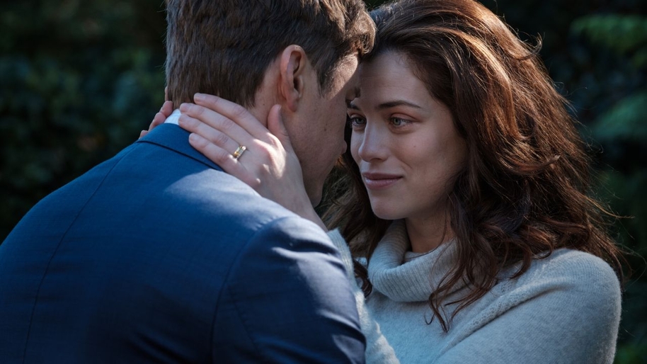 The back of aman in a blue suit and a women with brown hair looking at him lovingly