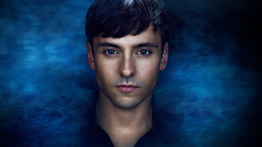 Close up of a man with brown hair and a blue water like background behind him