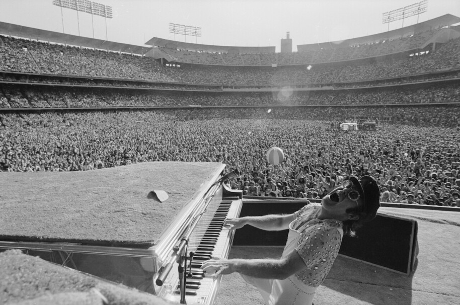 black and white photo of elton john performing on piano to arena