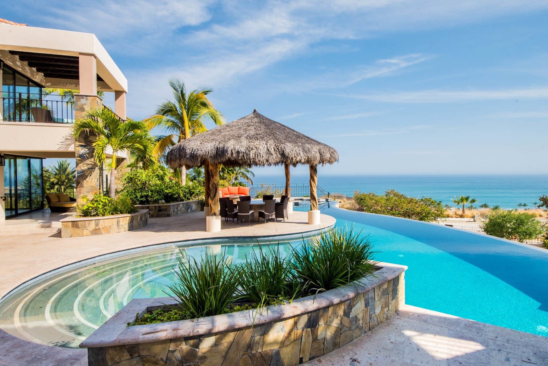 Luxury villa in Mexico overlooking cerulean ocean with palm-framed infinity pool.