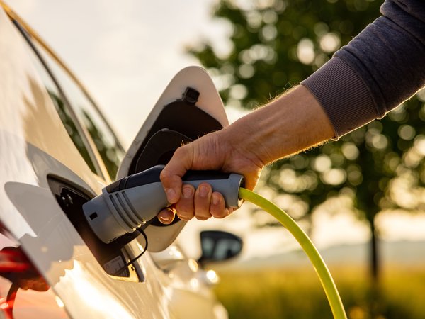 Man's hand holds a charger up to the socket of an electric vehicle