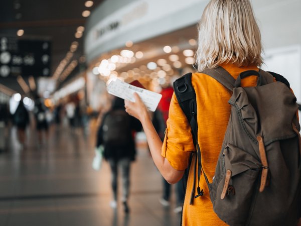 Blonde woman at airport with backpack holding an airplane ticket