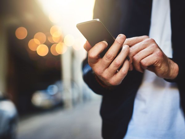 Man's hands hold and interact with a mobile phone. The man is standing on a city street