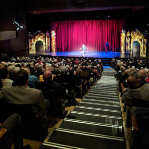 A performer on stage and seniors sitting in the theater audience