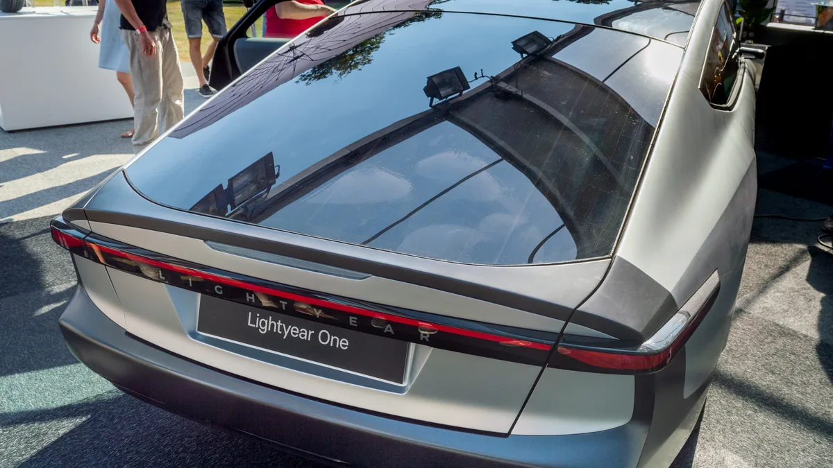 An aerodynamic electric vehicle featuring an integrated panoramic solar roof panel charging outdoors