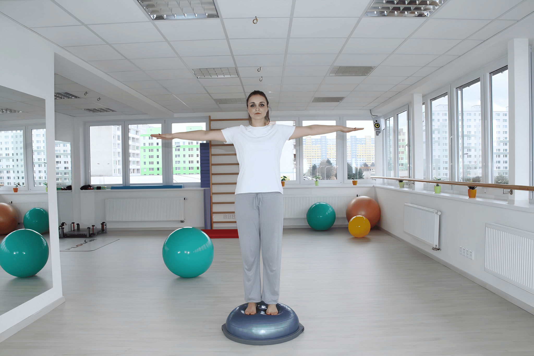 Žena stojí napřímeně na balanční podložce BOSU s upaženýma rukama – výchozí pozice cviku rotace trupu.
