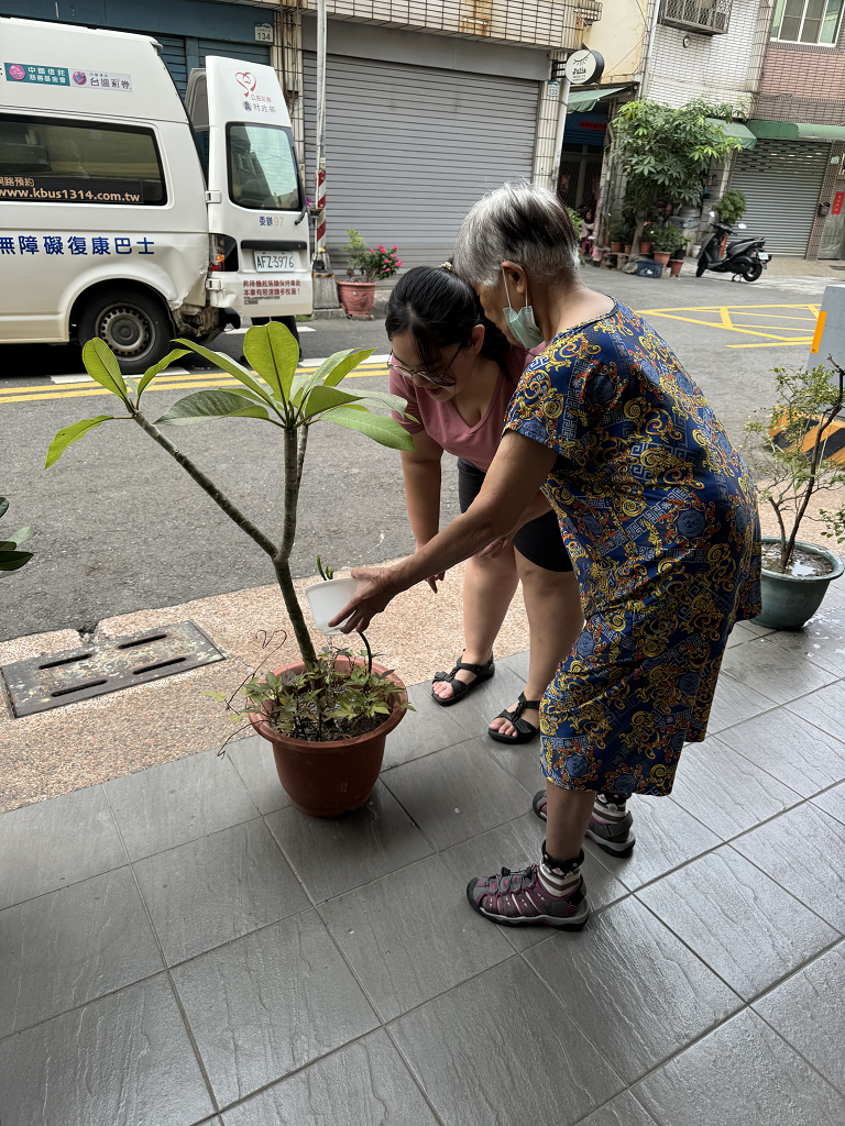 社工帶著長輩一起幫據點外的盆栽澆水。