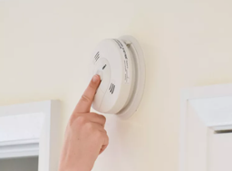 A hand reaches up to press the button on a carbon monoxide detector