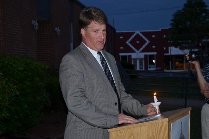District Attorney Jack Bostick standing at a podium with a lit candle.