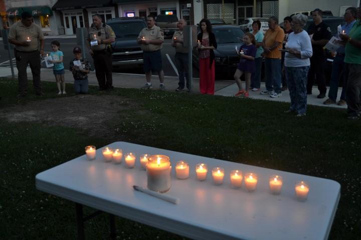 Table with the lit candles and vigil participants in the background.