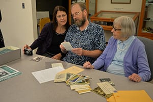 Ann (right) looks on as her son and daughter-in-law look over photos and documents.