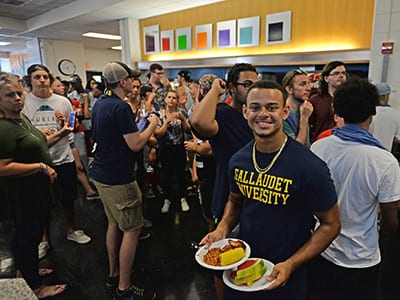A new student holds his plate full of BBQ food and smiles at the camera.