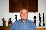 Joe Kinner in front of a mantle with various pieces behind him -- possibly African