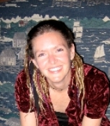 Raychelle Harris wearing a dark red top smiles at the camera. Behind her is a painting of sailboats on the water