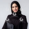 a beautiful young Arab female secretary dressed formally in black and wearing a hijab with a friendly expression and smile carrying a file-819527896