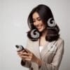 beautiful young Indonesian woman in formal clothes, looking at a cellphone screen with a cheerful expression-1254129543