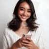 beautiful young Indonesian woman looking at a cellphone screen with a cheerful expression-330905848