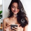 beautiful young Indonesian woman looking at a cellphone screen with a cheerful expression-692288