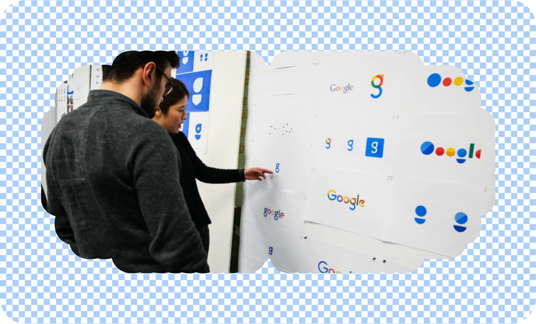 Two people review printed Google logo explorations pinned to a wall. One person points to a small "g" logo.
