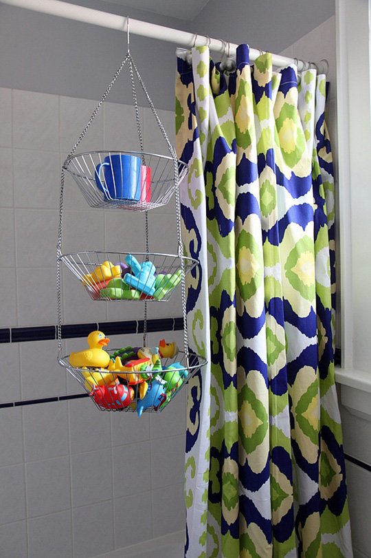 Tiered wire baskets hanging from a shower rod holding kids bathtub toys.