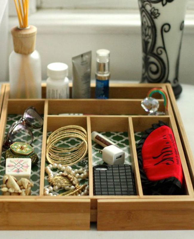 Wooden drawer organizer being used as a bedside valet for women's accessories.