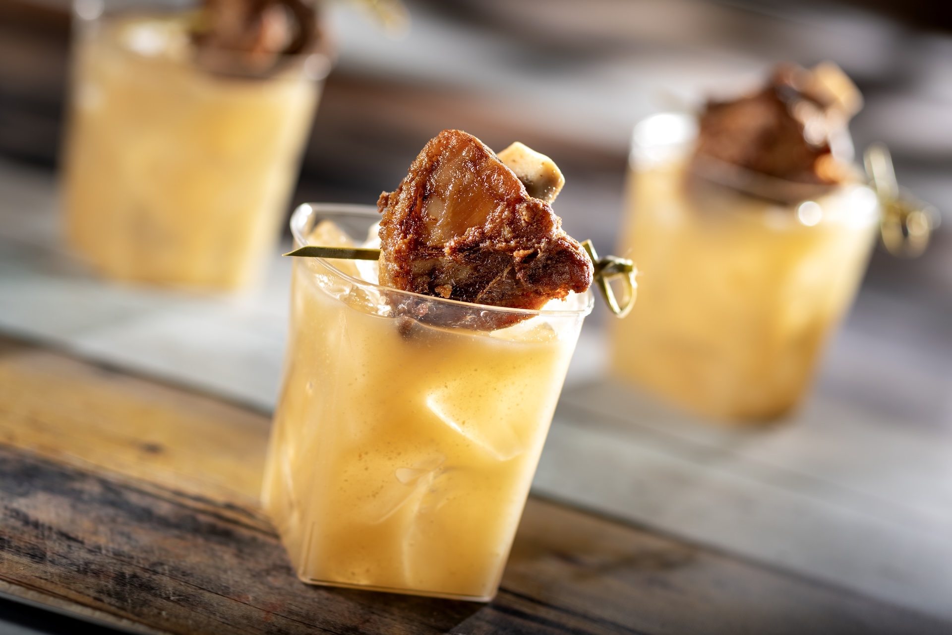 Swine Brine, Jim Beam Kentucky Straight Bourbon Whiskey, apple-cinnamon cider, lemon juice, and Dijon mustard topped with a pork wing, served at Flavors from Fire during the 2026 EPCOT International Food and Wine Festival