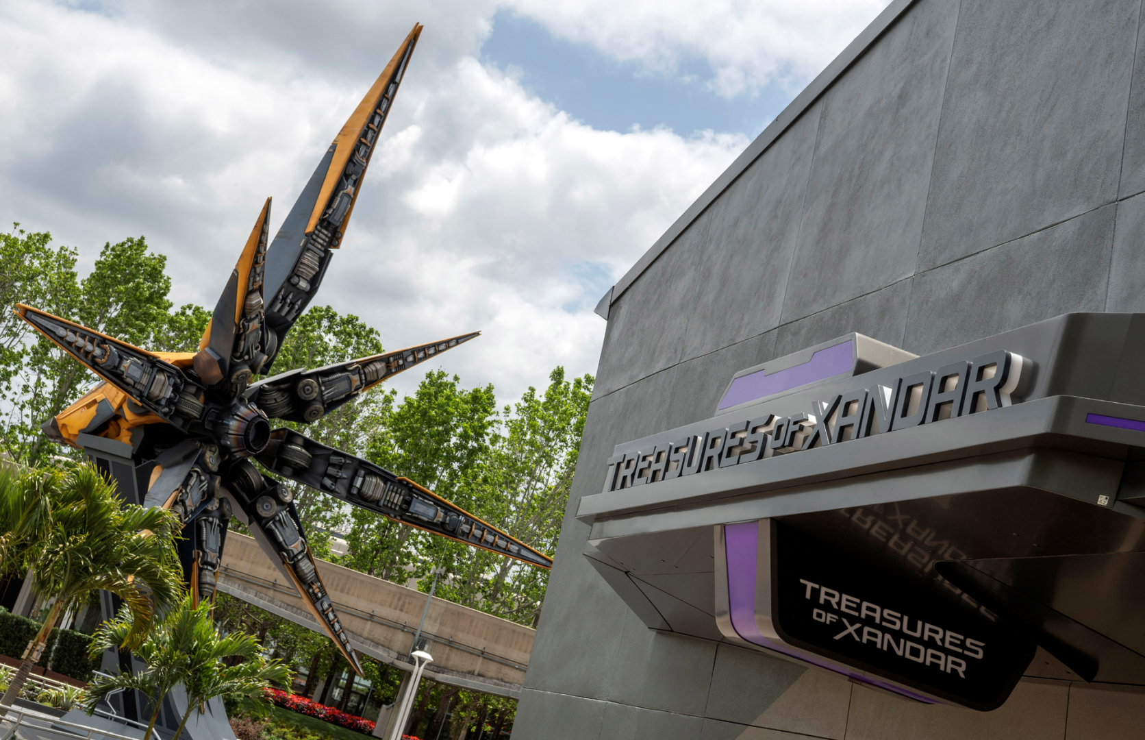 The Treasures of Xandar shop sign on a gray building, with the orange and black starship sculpture beside it