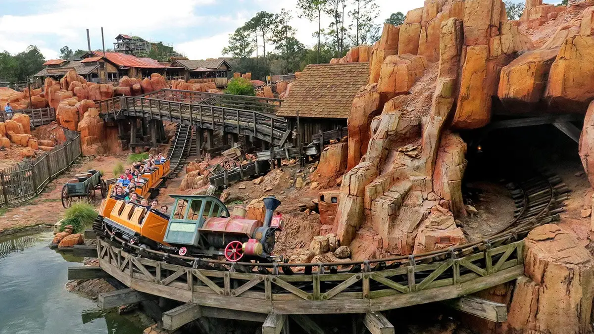 Guests riding Big Thunder Mountain Railroad past the red rock formations at Magic Kingdom