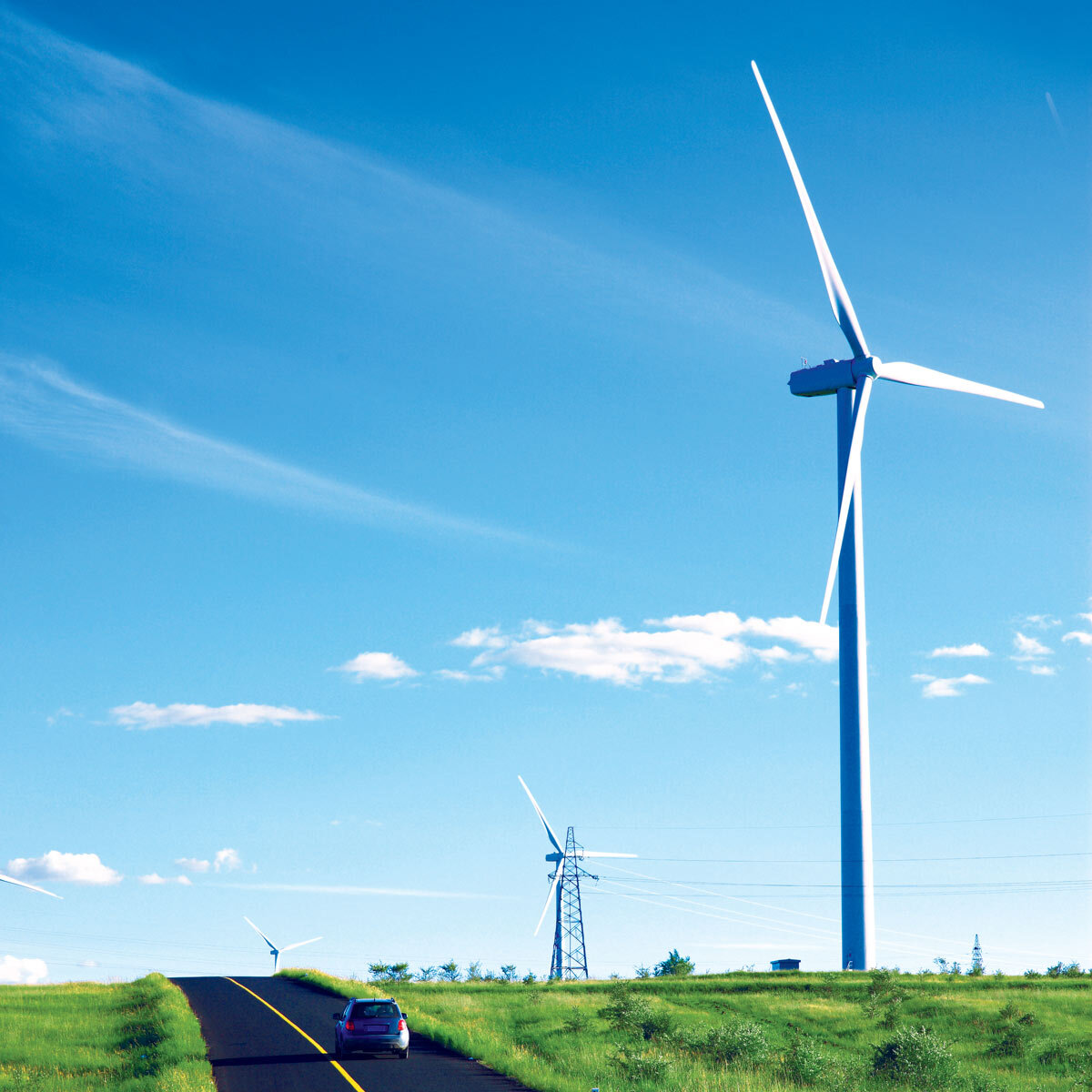 Car driving along the road with large wind turbines beside it