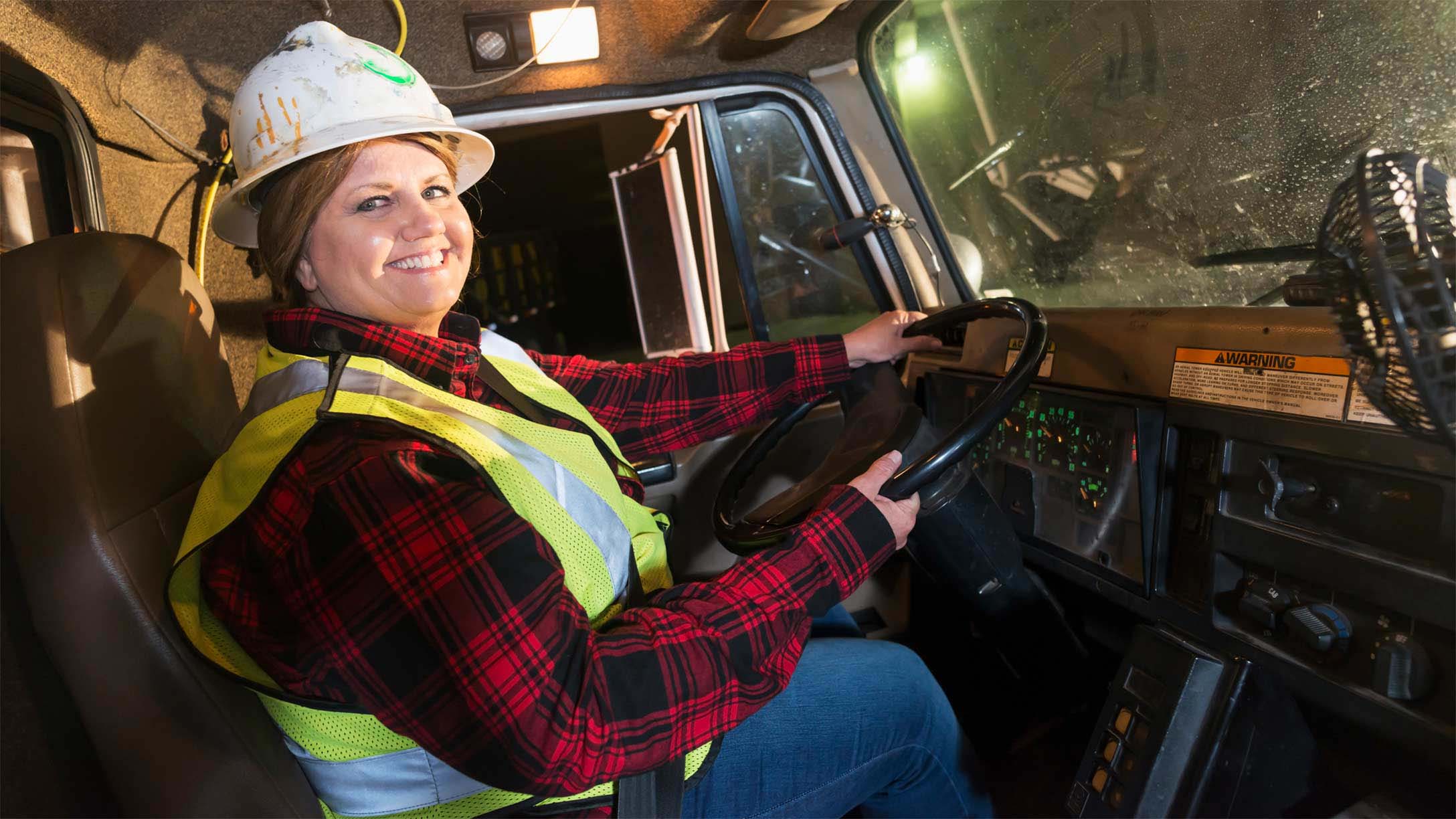 Woman wearing a vest and hardhat driving a truck