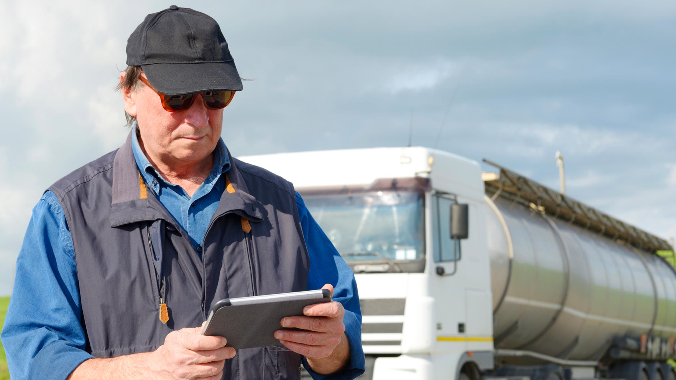 Man in a vest using an electronic logging device outside in front of a truck