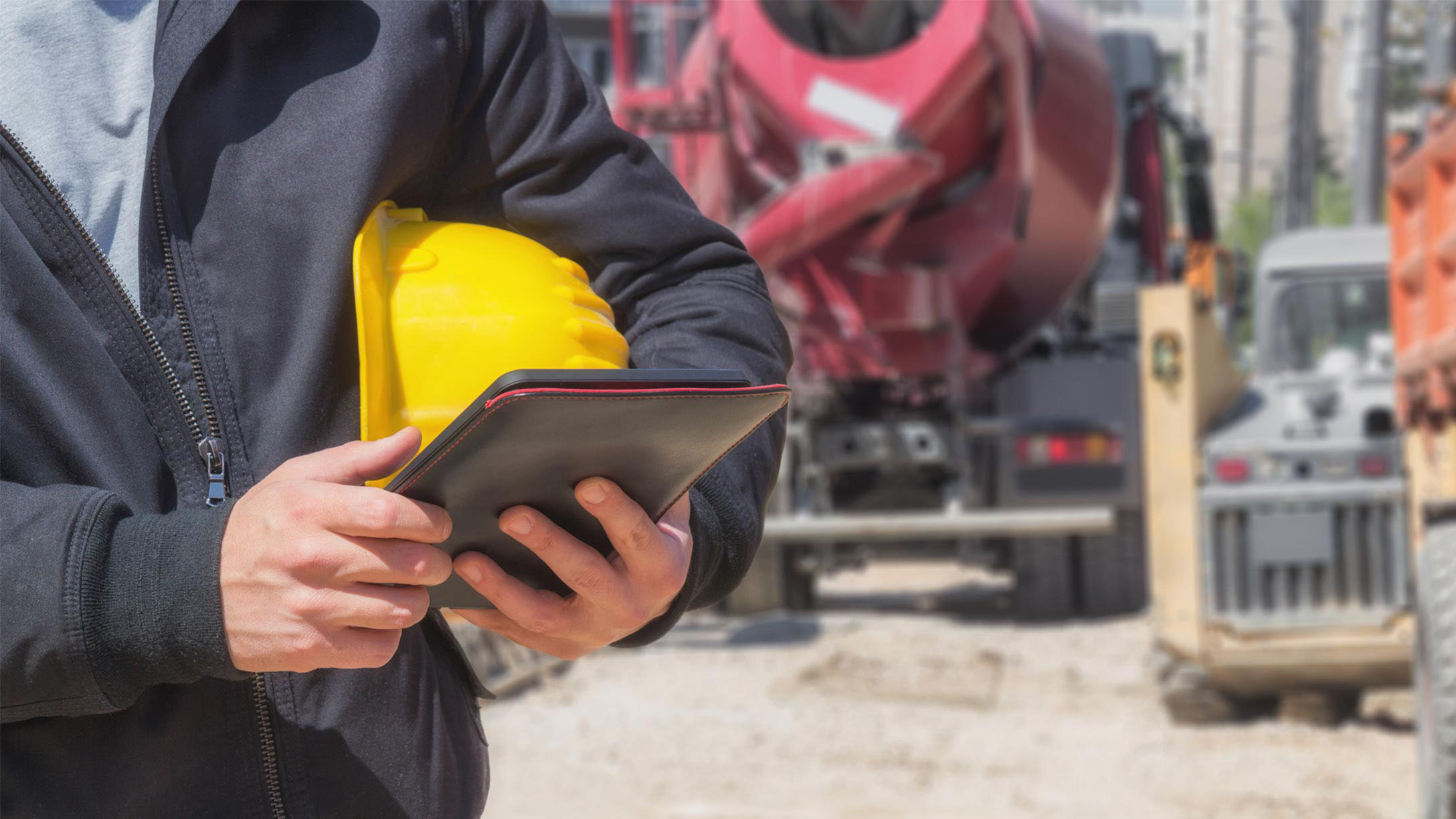 Man holding a hard hat and a tablet in front of trucks outside