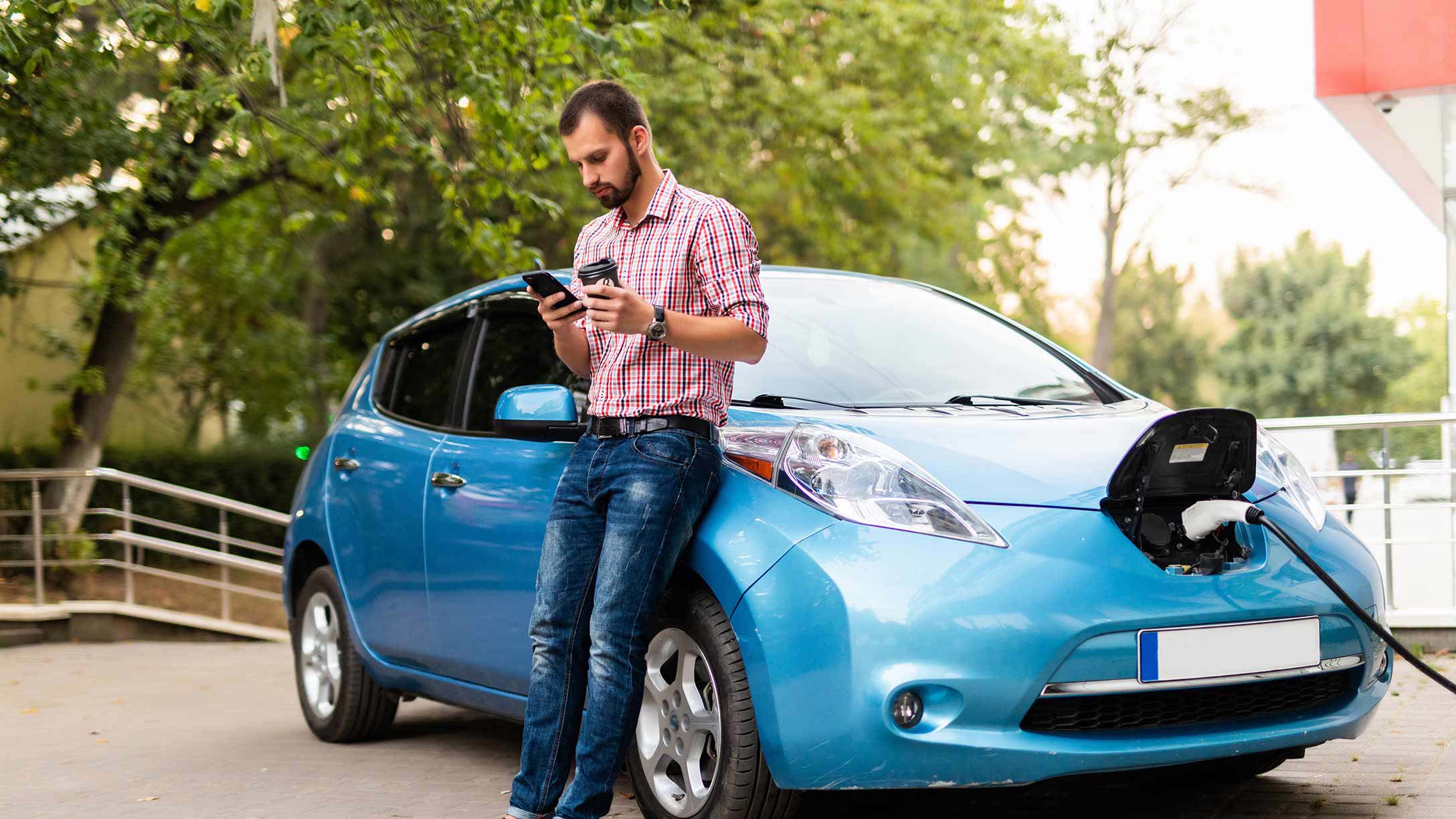Man in front of a charging electric vehicle while using their phone