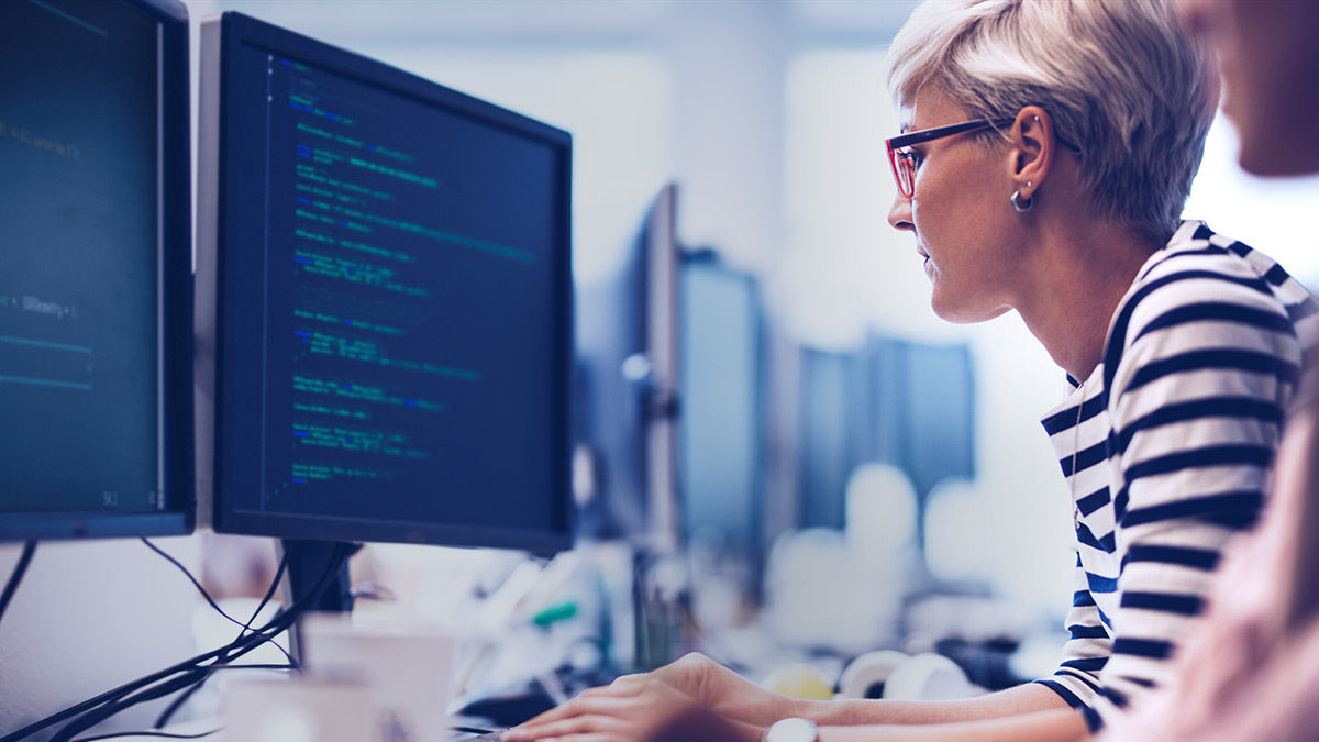 Placeholder Title A woman writing code, sitting in front of a computer monitor.