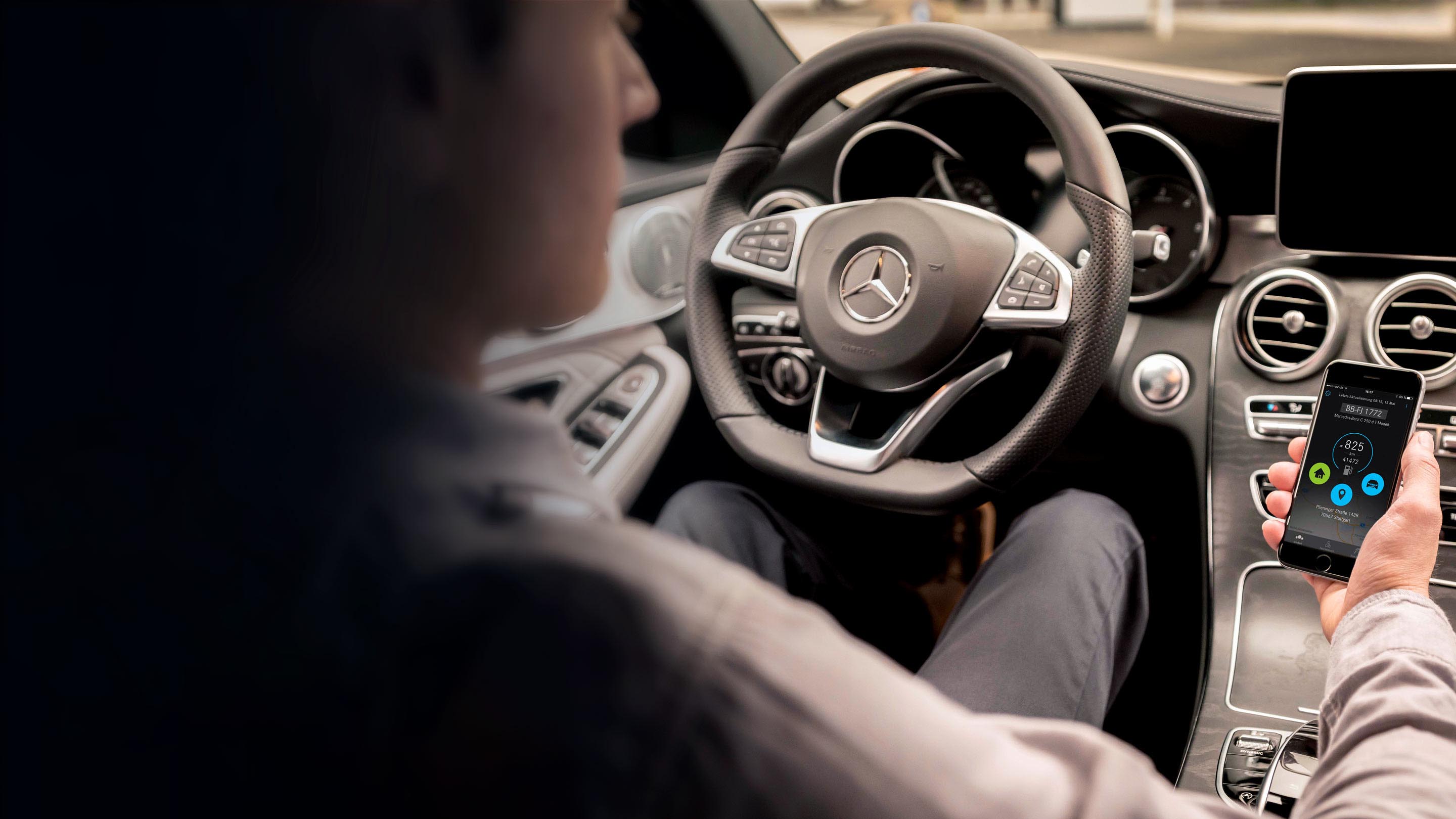 Person sitting in their vehicle using integrated platform for Mercedes-Benz on their phone
