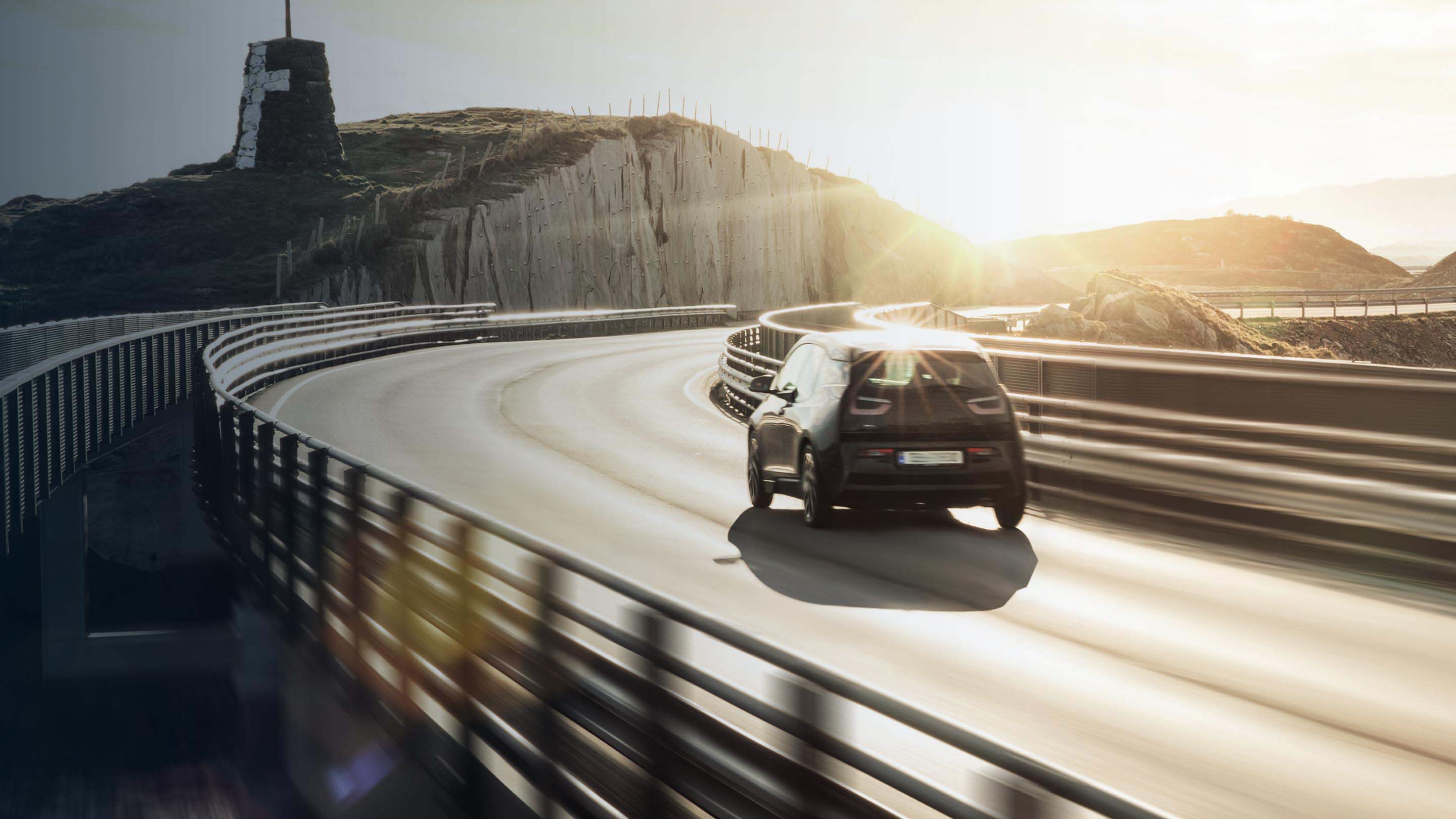 Black electric vehicle driving on road with sun reflecting against it